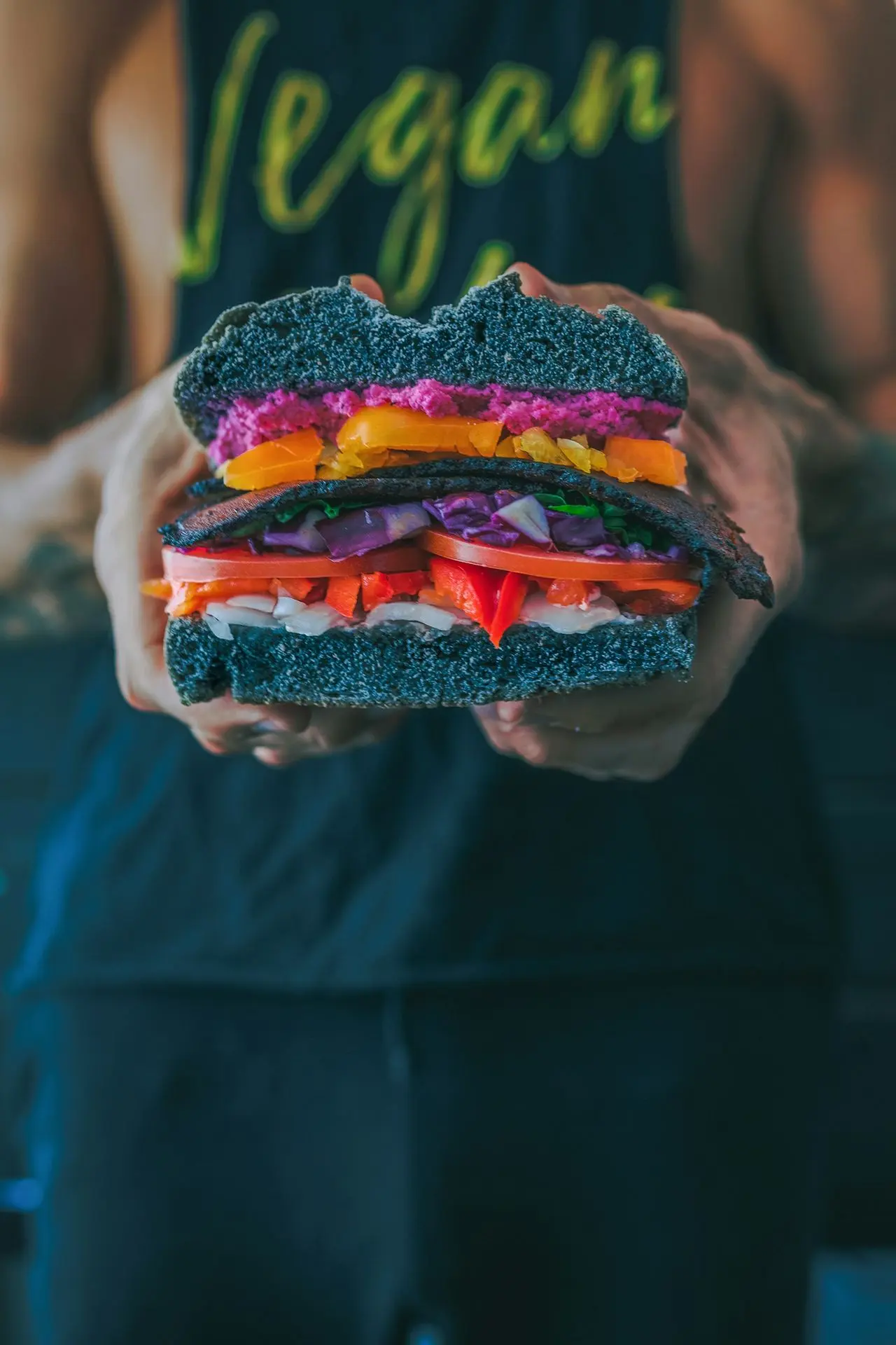 person holding vegan sandwich with sliced tomatoes, onions, and grilled meat